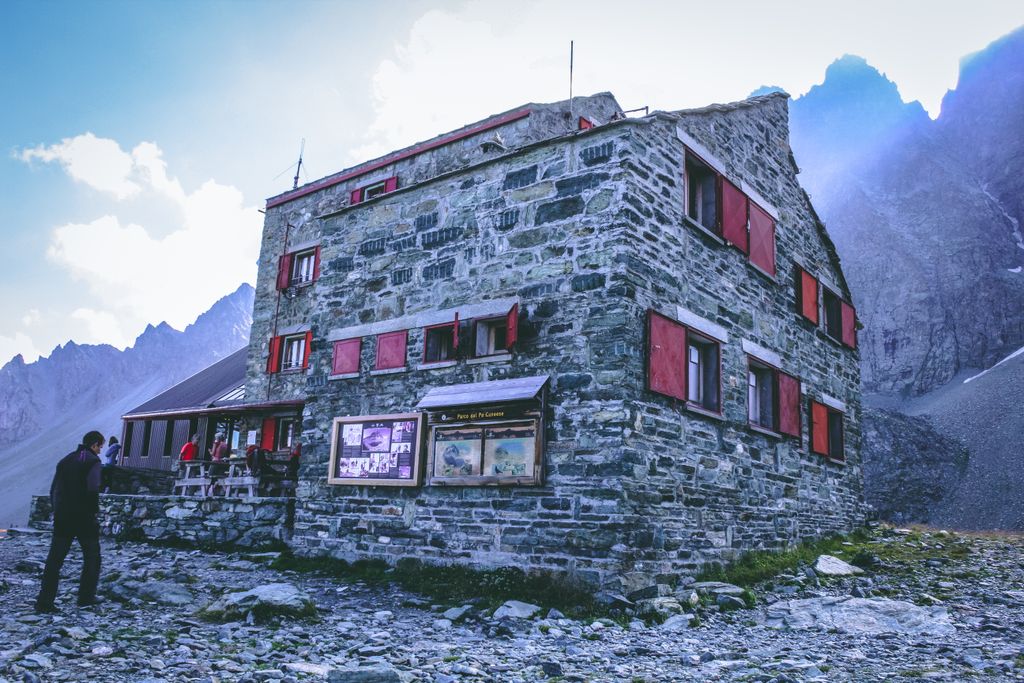 Berghütte aus Stein mit roten Fensterläden am Fuss der Gipfel